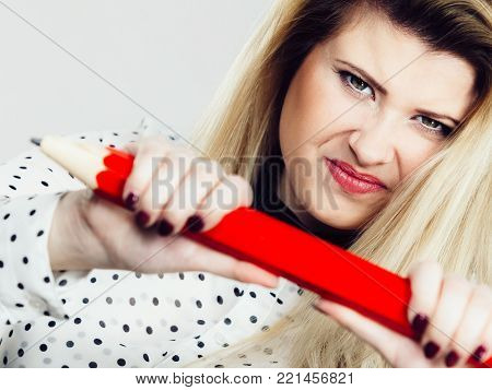 Angry mad woman blonde student girl or female teacher, Stressed business worker releasing tension by breaking big red pencil. Studio shot on grey