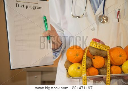 Slim down dieting concept. Doctor in white lab coat recommending healthy food. Doctor specialist dietitian holding fruit fruits and measure tape isolated. Fruit diet. Low-fat diet