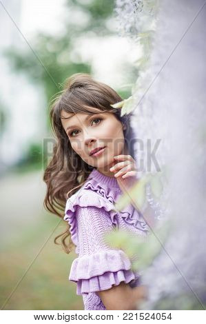 Portrait of a beautiful young brunette woman. A young woman is walking along the spring park. The girl is standing near the wisteria. Blooming park. Spring.