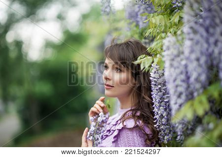 Portrait of a beautiful young brunette woman. A young woman is walking along the spring park. The girl is standing near the wisteria. Blooming park. Spring.
