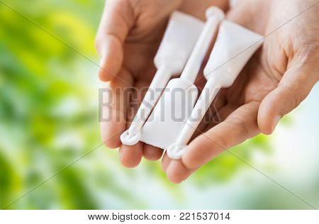 medicine, healthcare and pharmaceutics concept - hands holding tubes of micro enema over green natural background