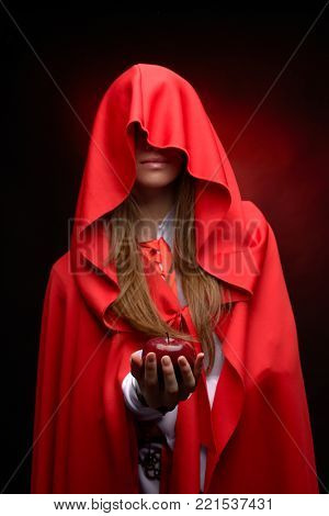 beautiful woman with res cloack holding red apple in studio