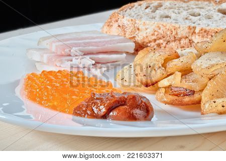 Tasty hazardous food. Greasy fried potatoes, bacon, red caviar, spicy sauce and white bread on a white plate. Russian snacking.