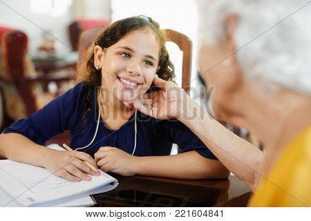 Happy little girl doing school homework with elderly woman at home. Family relationship with grandmother and granddaughter. Grandma teaching, female grandchild learning
