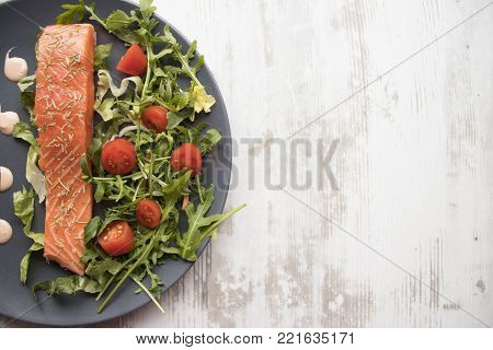 Appetizing salmon on a plate with sauce, arugula and cherry tomatoes on a wooden background