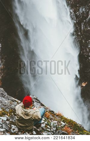 Man traveler sitting on cliff enjoying waterfall Vettisfossen view outdoor Travel Lifestyle concept adventure vacations in Norway roam wild nature