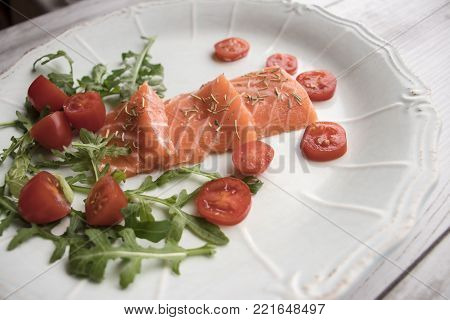 Tasty salmon on a plate with arugula and cherry tomatoes on a wooden background.