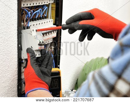 Young electrician technician fixes the electric cable to the magnetothermic switch with the screwdriver