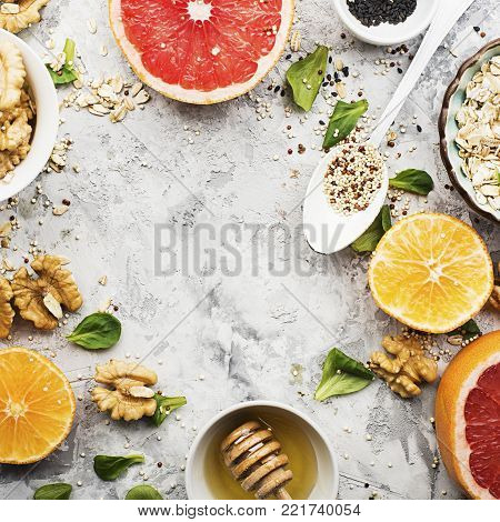 Ingredients of healthy breakfast food: oat flakes, kinoa, walnuts, floral honey, greens, oranges, bloody grapefruits on a light marble background. Top View