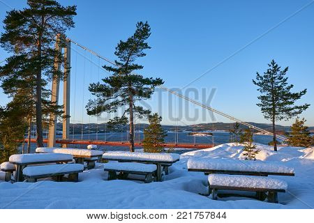 View at Hoga kusten bridge in winter in Sweden. Tourist benches and tables covered with snow.