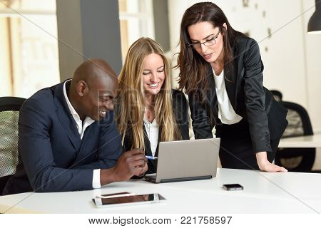 Multi-ethnic group of three businesspeople meeting in a modern office. Two caucasian women and a black man wearing suit looking at a laptop computer.