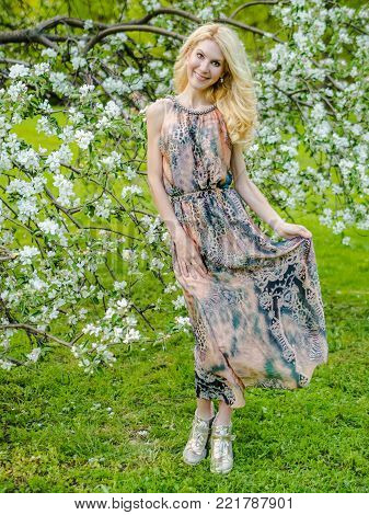 beautiful Russian girl blonde in a summer tight-fitting dress against the background of a blossoming apple tree