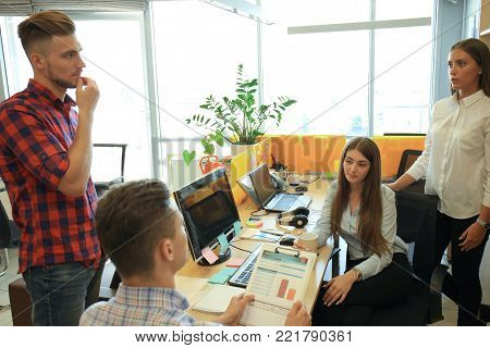 Group of young modern people in smart casual wear having a brainstorm meeting while standing in the creative office