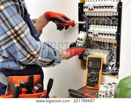 Young electrician technician introduces the electric cable into the clamp of the magnetothermic switch with an insulated clamp