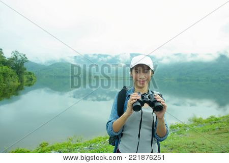 Thai adventure girl happy and holding a binoculars  with the lake background
