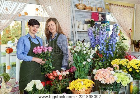 Women flower sellers. Two attractive young women working in flower shop and enjoying in beautiful flowers. Female sales assistant working as florist and holding bouquet with with roses.