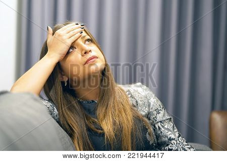 A sad young brunette woman sitting on the couch at home, she is depressed and lonely. The concept of loneliness and loss of love.
