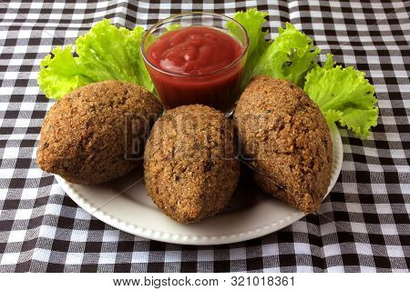 Kibbeh Fried With Tomato Sauce On A Plate, On Table Lined With Checkered Tablecloth