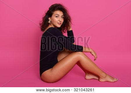 Woman With Perfectly Shaped Body Sitting On Floor And Holding One Hand On Her Leg And Touching Her D