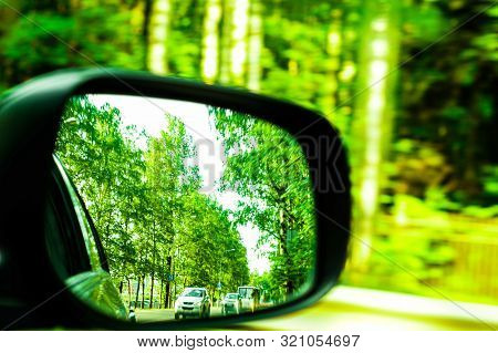 Car Mirror Reflects Green Trees Along The Road.