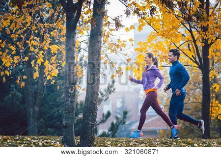 Woman and man jogging or running in park during autumn on a hill