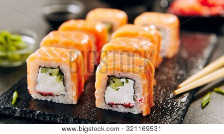 Beautiful Philadelphia Sushi Rolls Set with Salmon and Cream Cheese, Tobiko and Cuccumber on Black Slate Plate Close Up. Uramaki, Nori Maki or Futomaki Sushi with Trout Fillets, Soy Sauce and Wasabi