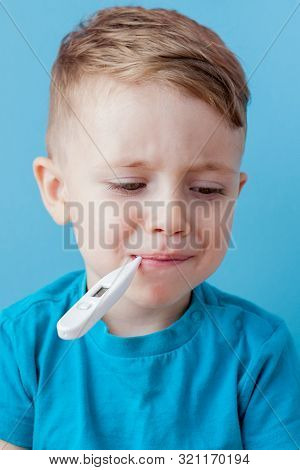 Ill Young Child With A Thermomether, Measuring The Height Of His Fever And Looking Into The Camera