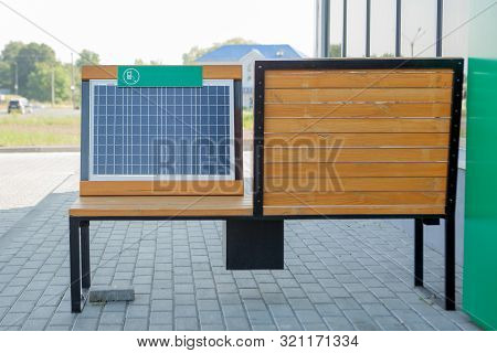 Outdoor Shot Of Wooden Bench In Park Having Solar Power Panel Installed, Usb Cabel Connected To Smar