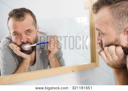 Adult Man Brushing His Teeth Looking At His Bathroom Mirror During Morning Hygiene Routine Being Bor