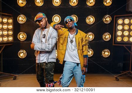 Two black rappers in caps, artists poses on stage