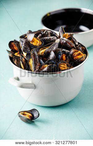 Pot full of steamed mussels on blue background