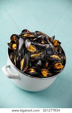 Pot full of steamed mussels on blue background