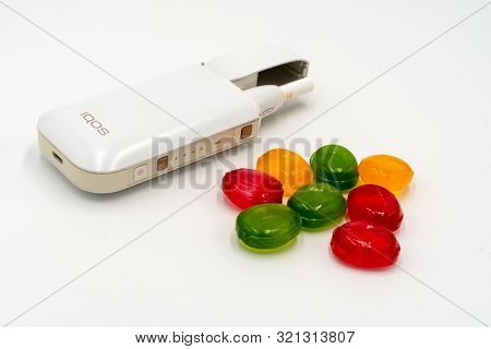 White Box Iqos And Multicolored Sweet Candy Lollipops On A White Background. The Concept Of Banning 