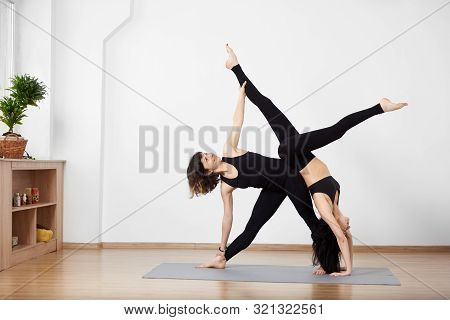 Two Slender Sporty Smiling Women Doing Complex Yoga Exercise On Mat And Showing Performing With Exte