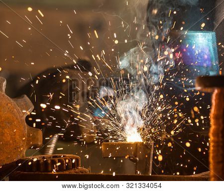 Welder is welding metal part in industrial workshop.