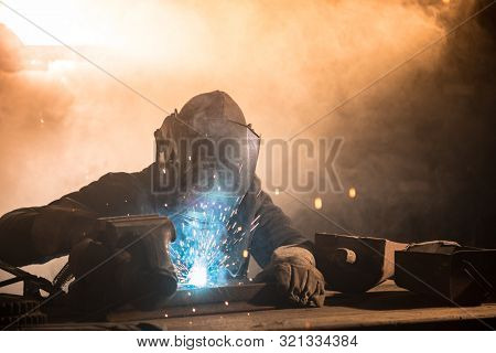 Welder is welding metal part in industrial workshop.