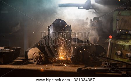 Welder is welding metal part in industrial workshop.
