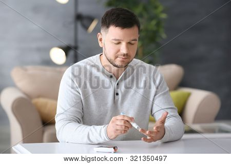 Diabetic man taking blood sample with lancet pen at home