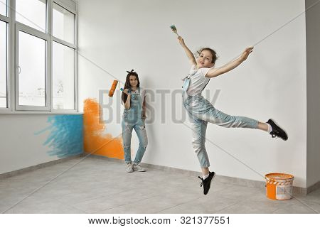 The Girls Paint The Walls. Friendly Collaboration Between The Two Sisters. Teens In Blue Overalls Ma
