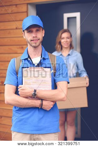 Smiling Delivery Man In Blue Uniform Delivering Parcel Box To Recipient - Courier Service Concept. S