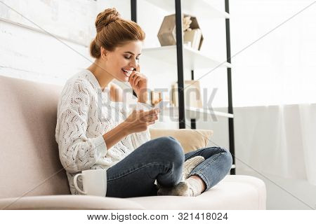 Attractive Woman In White Sweater Smiling And Using Smartphone