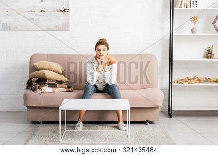 Attractive Woman In White Sweater Looking At Camera And Sitting On Sofa
