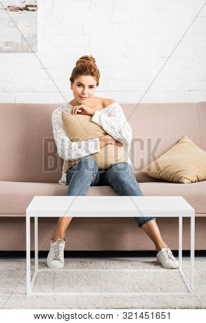 Attractive Woman In White Sweater Holding Pillow And Looking At Camera