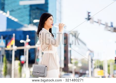 lifestyle and people concept - young asian woman drinking water flom plastic bottle in city