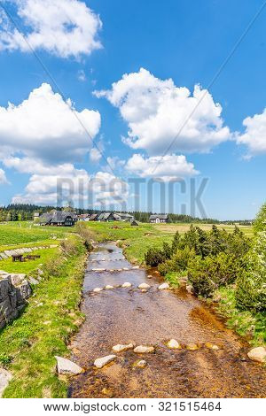 Sunny Summer Day In Jizerka Mountain Village. Jizerka River, Green Meadows And Blue Sky With White C