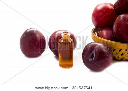 Raw Organic Red Ripe Plums In A Brown-colored Basket Along With Its Extracted Essential Oil In A Sma