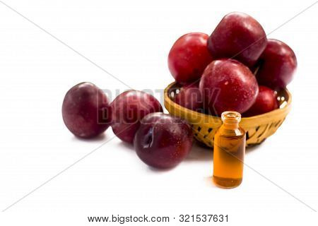Raw Organic Red Ripe Plums In A Brown-colored Basket Along With Its Extracted Essential Oil In A Sma