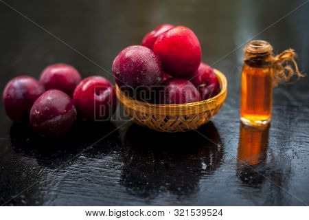Raw Organic Red Ripe Plums In A Brown-colored Basket Along With Its Extracted Essential Oil In A Tra