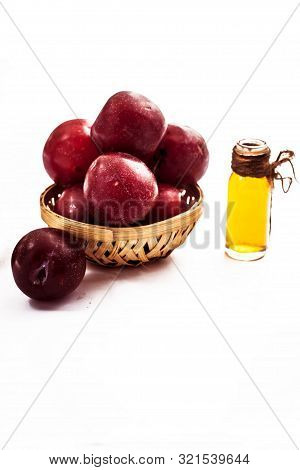 Raw Organic Red Ripe Plums In A Brown-colored Basket Along With Its Extracted Essential Oil In A Tra