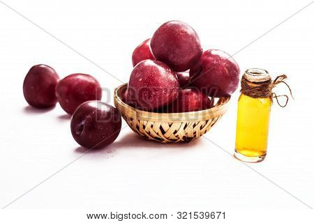 Raw Organic Red Ripe Plums In A Brown-colored Basket Along With Its Extracted Essential Oil In A Tra